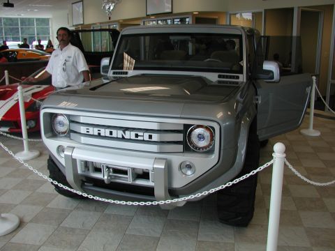 1985 Ford Bronco - A silver Ford Bronco concept vehicle is displayed indoors with its driver's door open.