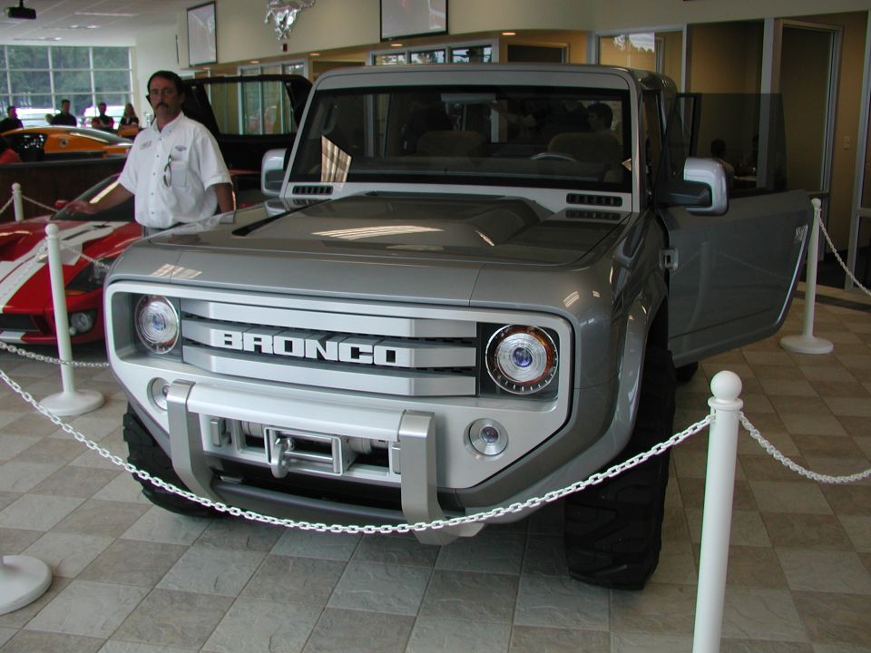 Silver Ford Bronco concept with "BRONCO" text on grille, open driver's door, and winch