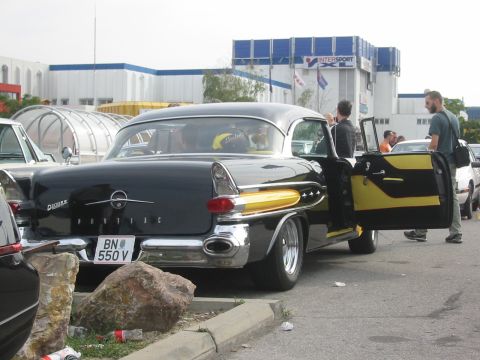 1992 Ford Crown Victoria - A black 1957 Pontiac Star Chief with distinctive yellow side accents and an open driver's door is parked outdoors.