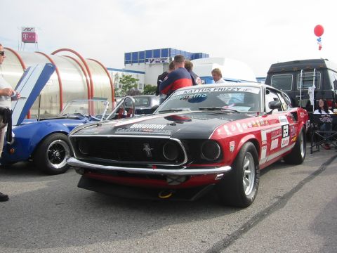 1992 Ford Crown Victoria - A vintage Ford Mustang race car is parked on asphalt, with a blue convertible and people in the background.