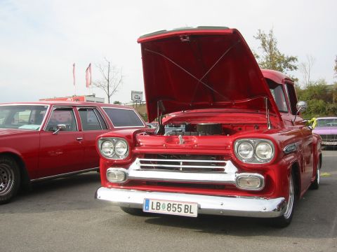 1992 Ford Crown Victoria - A red 1958 Chevrolet Apache pickup truck is parked next to a red station wagon, with its hood open.