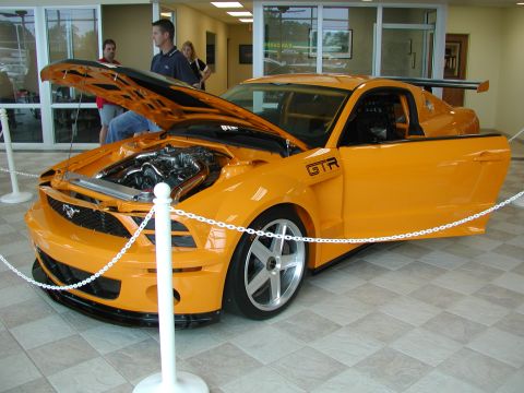 1985 Ford Bronco - Custom orange sports car with engine exposed and door open, displayed indoors.