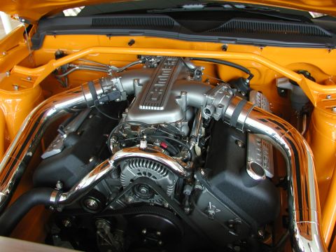 1985 Ford Bronco - Close-up view of a modified V8 engine bay with custom chrome piping and an orange strut tower brace.