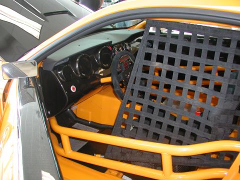 1985 Ford Bronco - The interior of a yellow race car is visible, a roll cage and a black racing net.