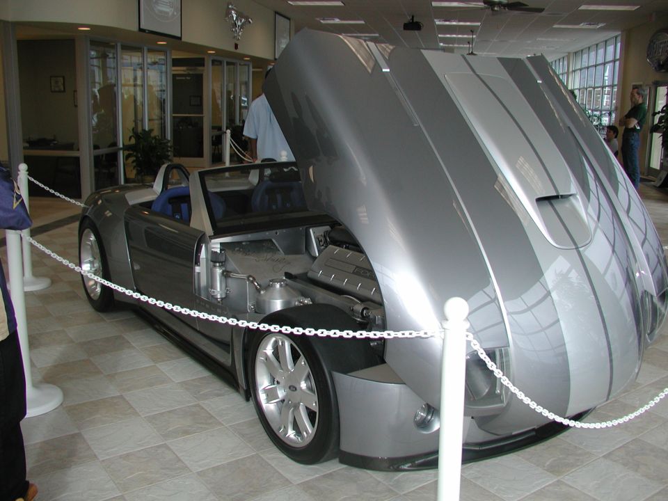 Silver convertible with hood open, showing engine and racing stripes