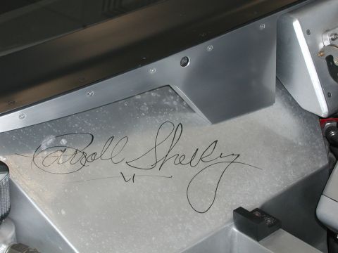 1985 Ford Bronco - Close-up of a metal panel with Carroll Shelby's signature and "SUPERMOTORS.NET" logo.