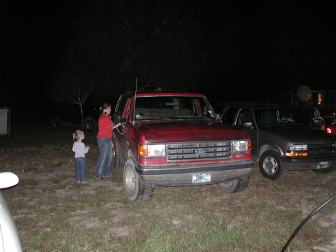 1985 Ford Bronco - Two trucks parked outside at night, one red Bronco and one silver pickup.