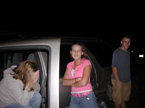 1985 Ford Bronco - Three people are gathered around a silver SUV at night, with one person partially inside the vehicle.