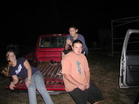 1985 Ford Bronco - People gathered around a red pickup truck and a silver SUV at night.