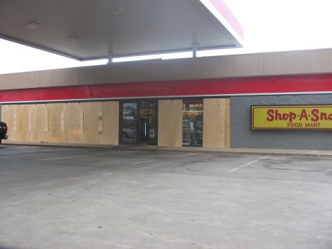 1988 Ford Bronco - A gas station storefront shows damage with plywood covering the windows, except for the entrance area.