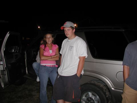 1985 Ford Bronco - A silver SUV is parked outdoors at night with several people standing around it.