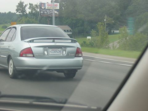 1988 Ford Bronco - A silver sedan drives on the highway, its rear visible with a spoiler and license plate.