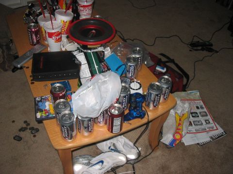 1988 Ford Bronco - A coffee table is covered in cans of Bud Light, fast food cups, a car stereo speaker, and various electronic devices.