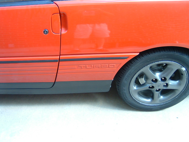 Red car side detail with TURBO stripe graphic, black lower cladding and dark alloy wheel