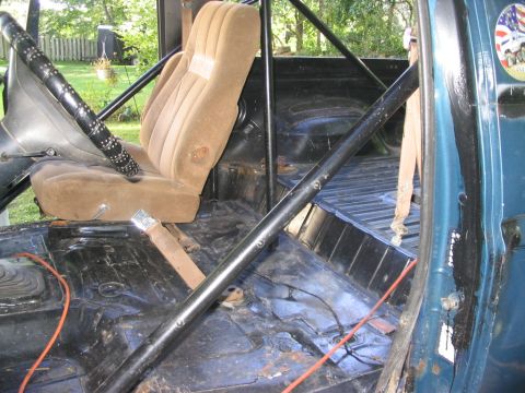 1986 Ford Bronco - The interior of a truck shows a roll cage, a single bucket seat, and wiring on the floor.