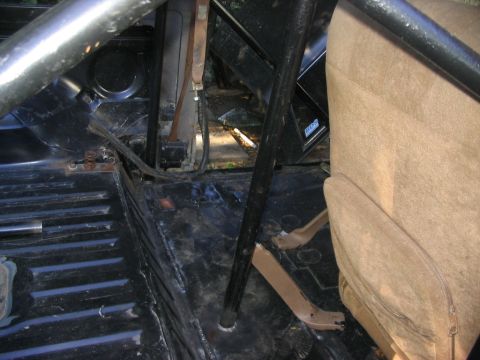 1986 Ford Bronco - The interior of a vehicle is visible, a roll cage and a tan seat, with floor pedals in view.