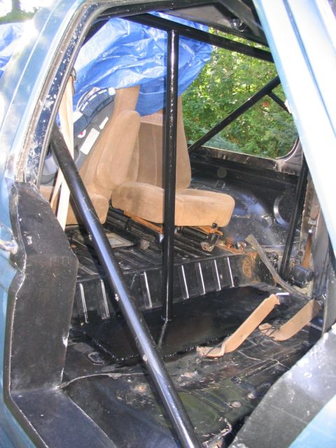 1986 Ford Bronco - The interior of a vehicle shows a roll cage and tan seats, with a blue tarp partially covering the back.