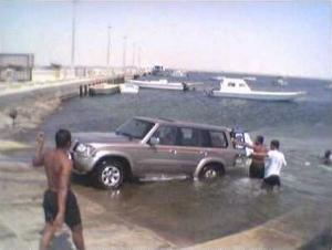 1993 Ford Bronco - A silver SUV is partially submerged in the water near a dock with several boats in the background.