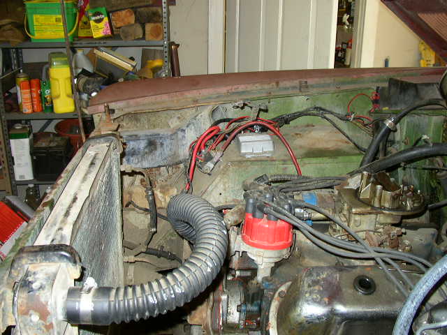 Engine bay with radiator, distributor, and carburetor visible. Rusty metal and wiring are prominent