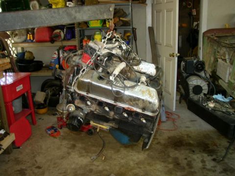 1995 Ford Bronco - An engine is hoisted by chains in a cluttered garage setting, with tools and shelves visible in the background.