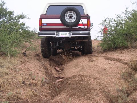 1990 Ford Bronco - The rear view of a lifted Ford Bronco navigating a rough, dry creek bed.