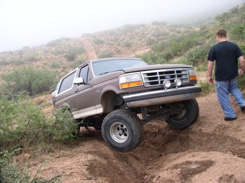 1990 Ford Bronco - A brown 1990 Ford Bronco navigates a steep dirt incline during an off-road excursion.