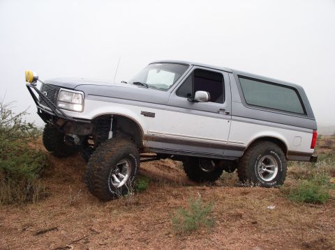 1990 Ford Bronco - Modified 1990 Ford Bronco navigating rough terrain with a custom front bumper and large tires.