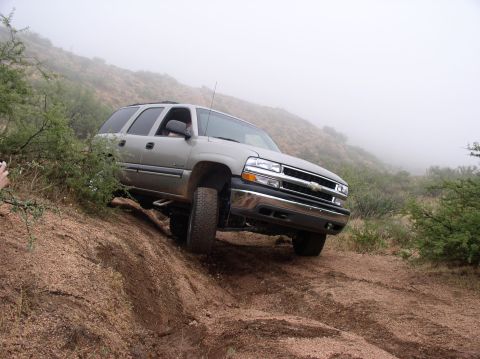 1990 Ford Bronco - This SUV is navigating a steep, muddy incline on a foggy day.