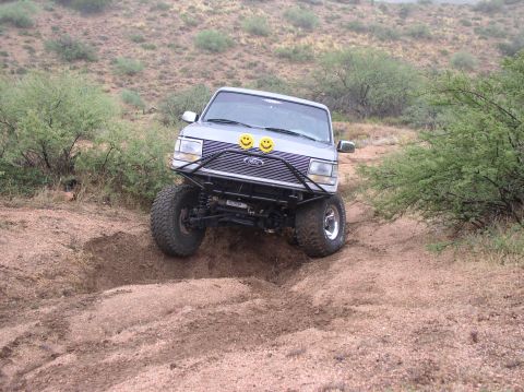 1990 Ford Bronco - A silver SUV navigates a challenging dirt terrain with its front end angled upwards.