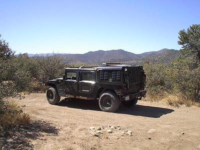 1988 Ford Bronco - A black Humvee is parked on a dirt road in a dry, mountainous area under a clear blue sky.