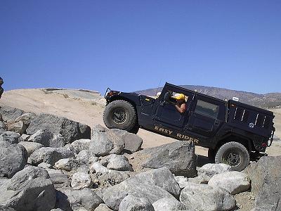 1988 Ford Bronco - A black Hummer H1 navigates a challenging rocky trail under a clear blue sky.