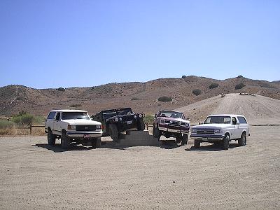 1988 Ford Bronco - Four-wheel drive vehicles gathered in a dusty, arid environment under a clear blue sky.