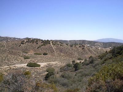 1988 Ford Bronco - A wide view of a dry, hilly terrain with scattered bushes and trees, and a clear sky above.