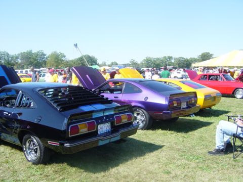 1978 Ford Mustang II - Several classic cars are parked on a grassy field under a clear blue sky at an outdoor event.