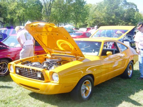 1978 Ford Mustang II - Yellow coupe with hood open at a car show, with other vehicles visible.