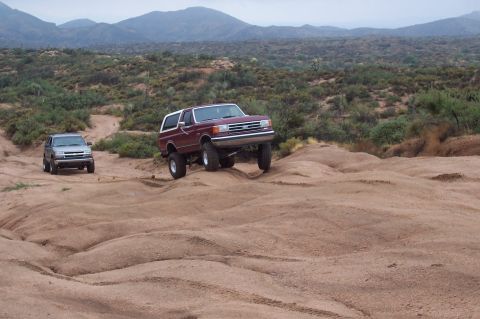 1992 Ford Bronco - Two SUVs navigate a rocky desert terrain under a cloudy sky.