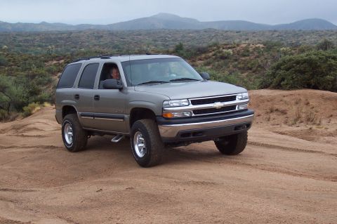 1992 Ford Bronco - This silver SUV, likely from the early 2000s, navigates a dusty, off-road trail with mountains in the background.