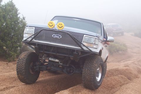 1992 Ford Bronco - A modified Ford truck navigates a foggy, off-road trail with another vehicle visible in the background.