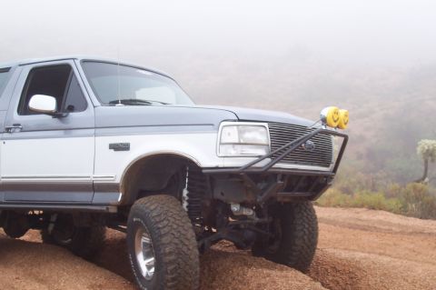 1992 Ford Bronco - This lifted 1992 Ford Bronco features a custom front bumper and unique smiley face auxiliary lights, seen in a hazy outdoor setting.