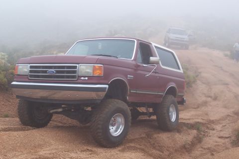 1992 Ford Bronco - 1992 Ford Bronco navigating a dusty, off-road trail with another vehicle visible in the fog.
