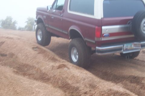 1992 Ford Bronco - This Ford Bronco is driving on a dirt path with some trees in the background.