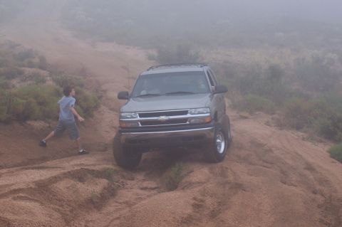 1992 Ford Bronco - A gray Chevrolet Tahoe navigates a dusty, off-road incline with a person walking nearby.