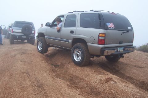 1992 Ford Bronco - A silver SUV navigates a dirt incline, with another SUV visible behind it in the fog.