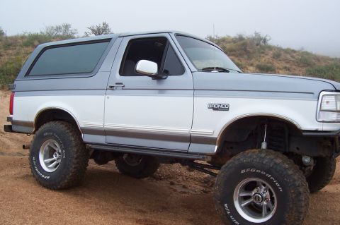 1992 Ford Bronco - A two-tone white and grey 1992 Ford Bronco is shown from a three-quarter front angle, lifted with off-road tires.