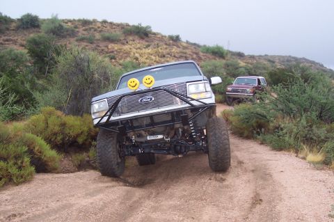 1992 Ford Bronco - Two Ford Broncos navigate an off-road trail in a dry, hilly landscape.