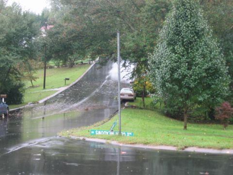 1985 Ford LTD Crown Victoria - A tan sedan is parked on the side of a flooded residential street with a street sign reading '21 Glen Meadows'.