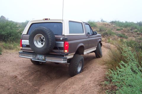 1992 Ford Bronco - 1992 Ford Bronco navigating an off-road trail with a spare tire on the back.