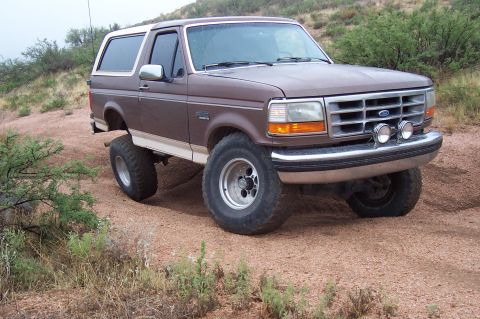 1992 Ford Bronco - 1992 Ford Bronco lifted for off-road use, parked on a dirt trail with scrub brush.