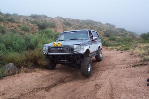 1992 Ford Bronco - A 1992 Ford Bronco navigates a dusty, off-road trail under foggy conditions.