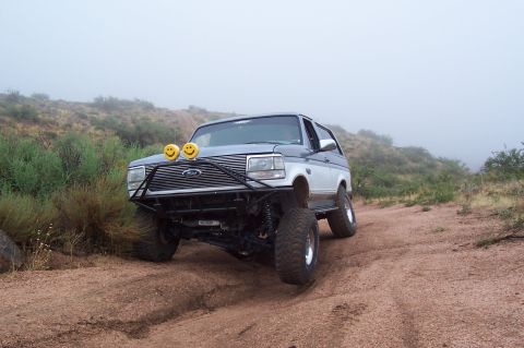 1992 Ford Bronco - Modified 1992 Ford Bronco navigates a dusty, off-road path with fog in the background.